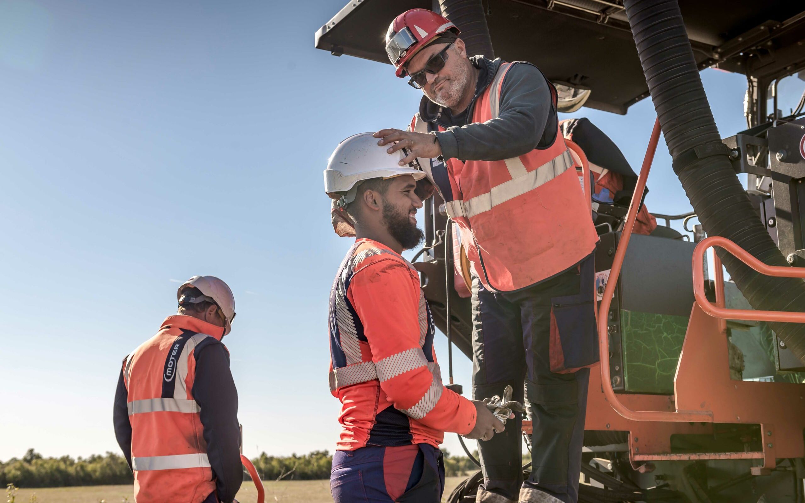 Photo de 3 compagnons Moter sur un chantier. Le chef d'équipe remet le casque d'un ouvrier